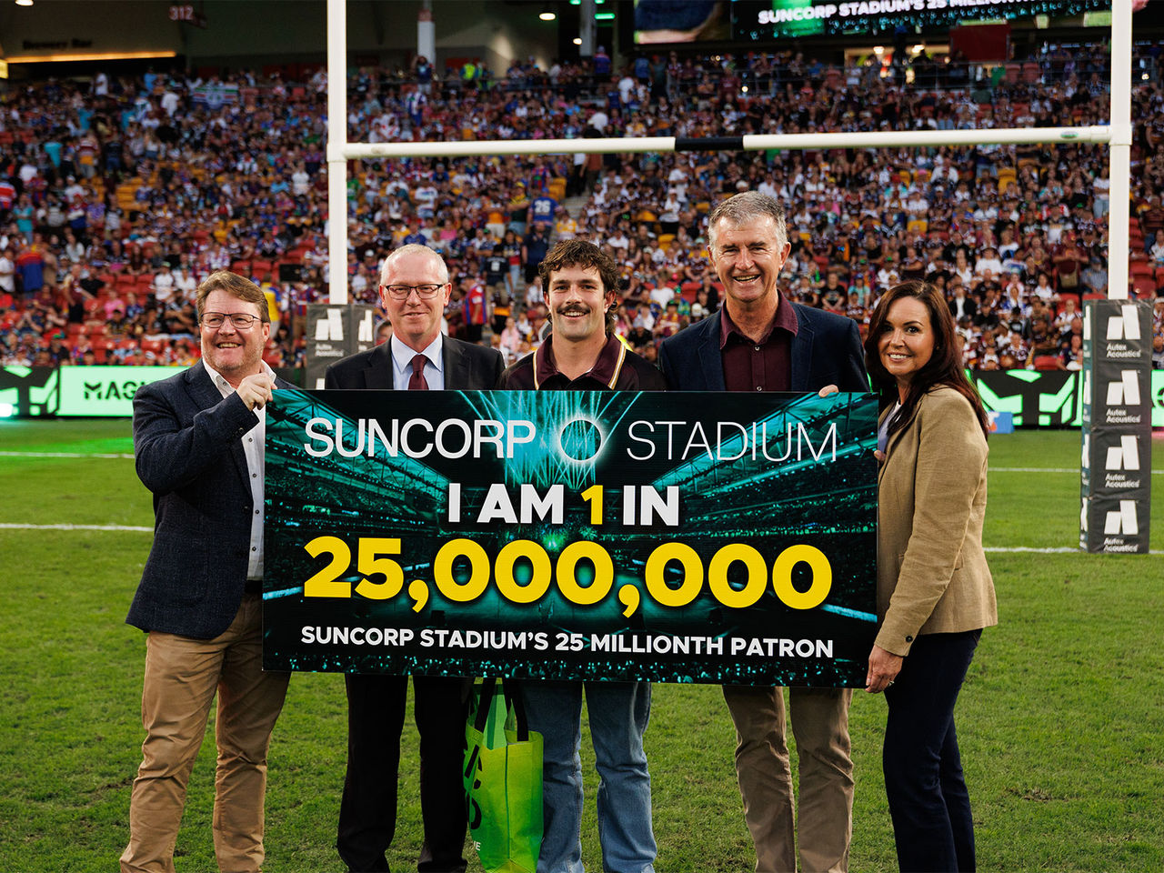 Todd Harris Stadiums Queensland CEO, Darren Burden Suncorp Stadium General Manager, Cormac the 25 millionth patron, The Hon Tim Mander Minister for Sport and Belinda Speirs Chief People Officer holding a sign for the 25 millionth patron