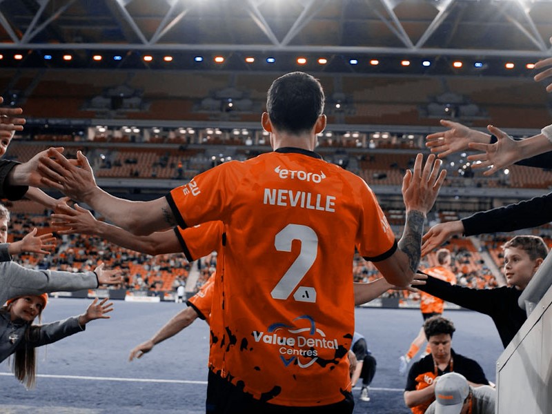 Brisbane Roar player Neville walking into a stadium whilst touching the hands of fans.