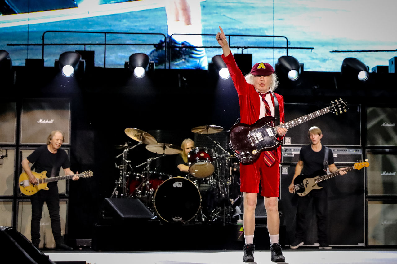 An image of an ACDC band member on stage holding up his hand