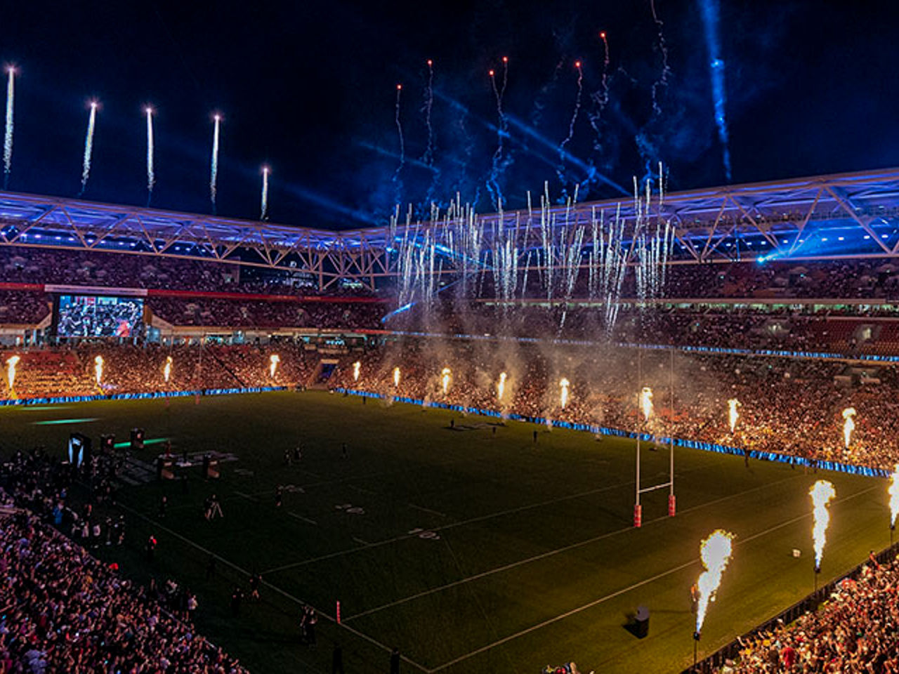 Image of a sold-out Suncorp Stadium during a nighttime event. Fireworks and other pyrotechnics on display.