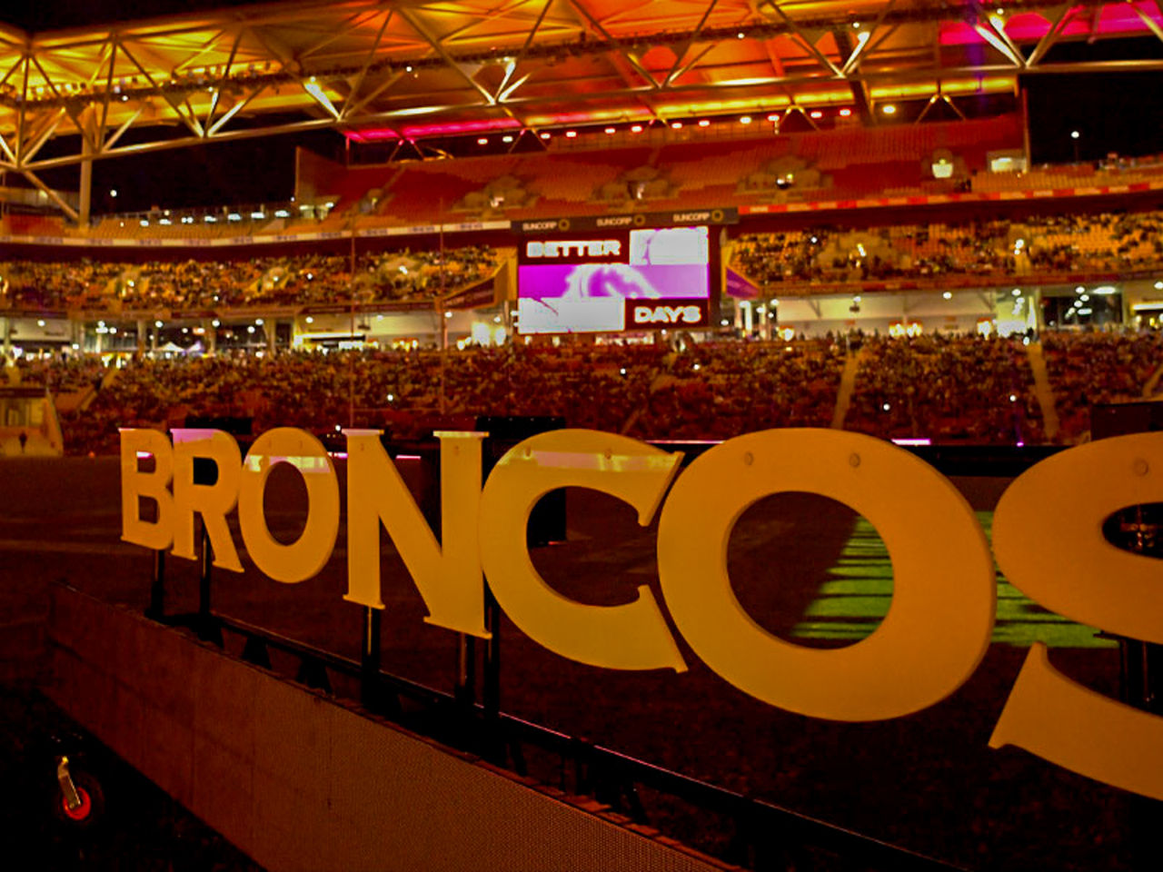 Broncos sign in front of Suncorp Stadium seating bowl during a nighttime event.