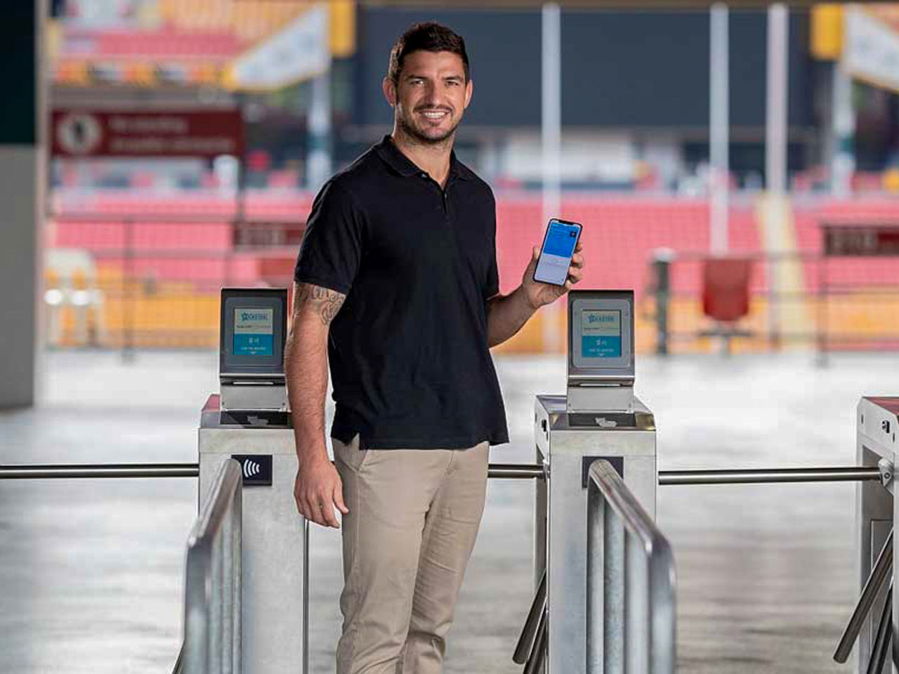 Image of a person standing in front of ticket scanners, smiling at camera, holding his phone up to show their contactless ticket.