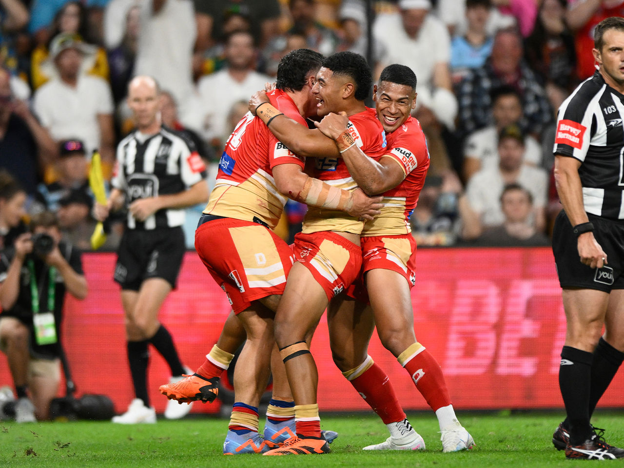 Image of three Dolphins players hugging each other, mid celebration, post try whilst on the Suncorp Stadium field.