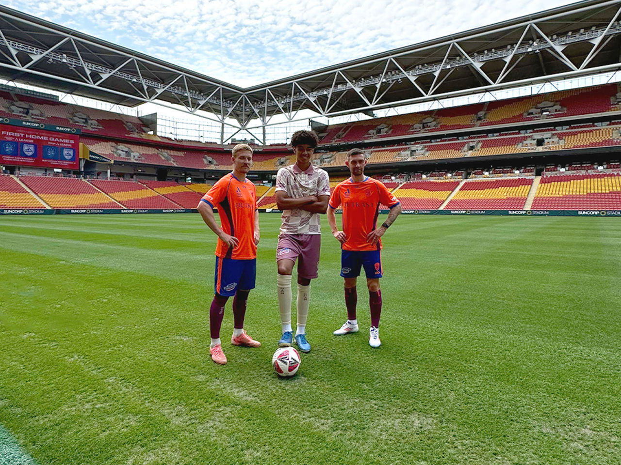 Three Brisbane Roar players posing on the field one with his foot on a soccer ball