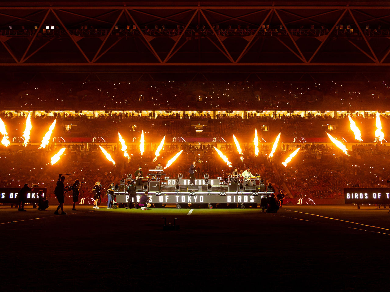 Birds of Tokyo performing at Suncorp Stadium at night-time. The stage is in the middle of the field with pyrotechnics going off around the band.