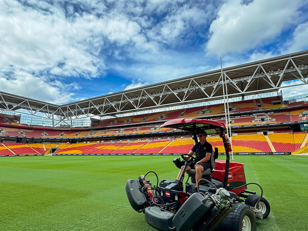 Image of staff member on lawn mower on Suncorp Stadium's field. Seating bowl is pictured in the foreground.