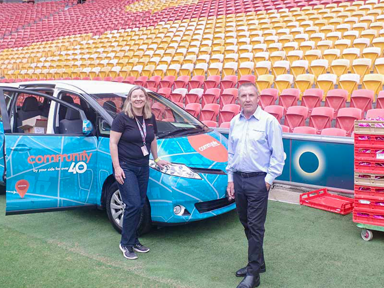 Image of a Communify representative (Left) and Simon Camp from the O’Brien Group (Right) on the Suncorp Stadium field close to the seating bowl. There is a Communify vehicle in the background.