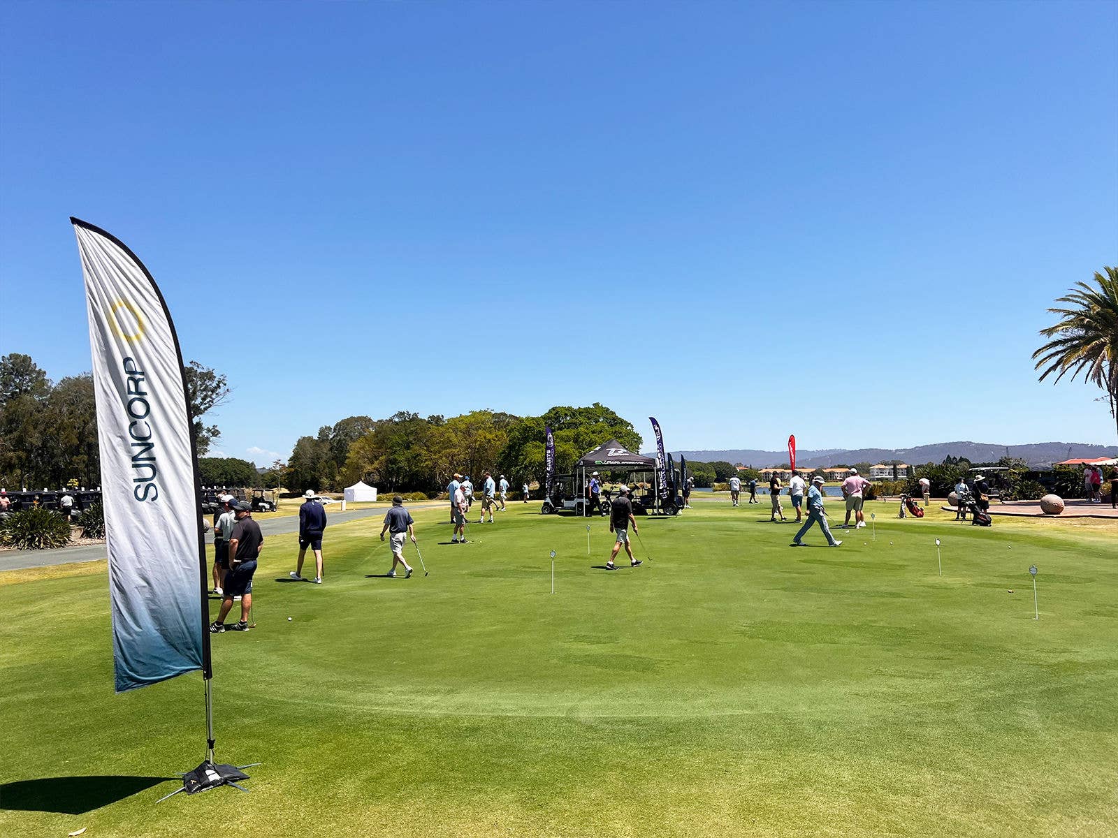 Links Hope Island golf course on a sunny day. Suncorp flag in foreground of image. Participants of the Suncorp Stadium golf day are walking on the course.