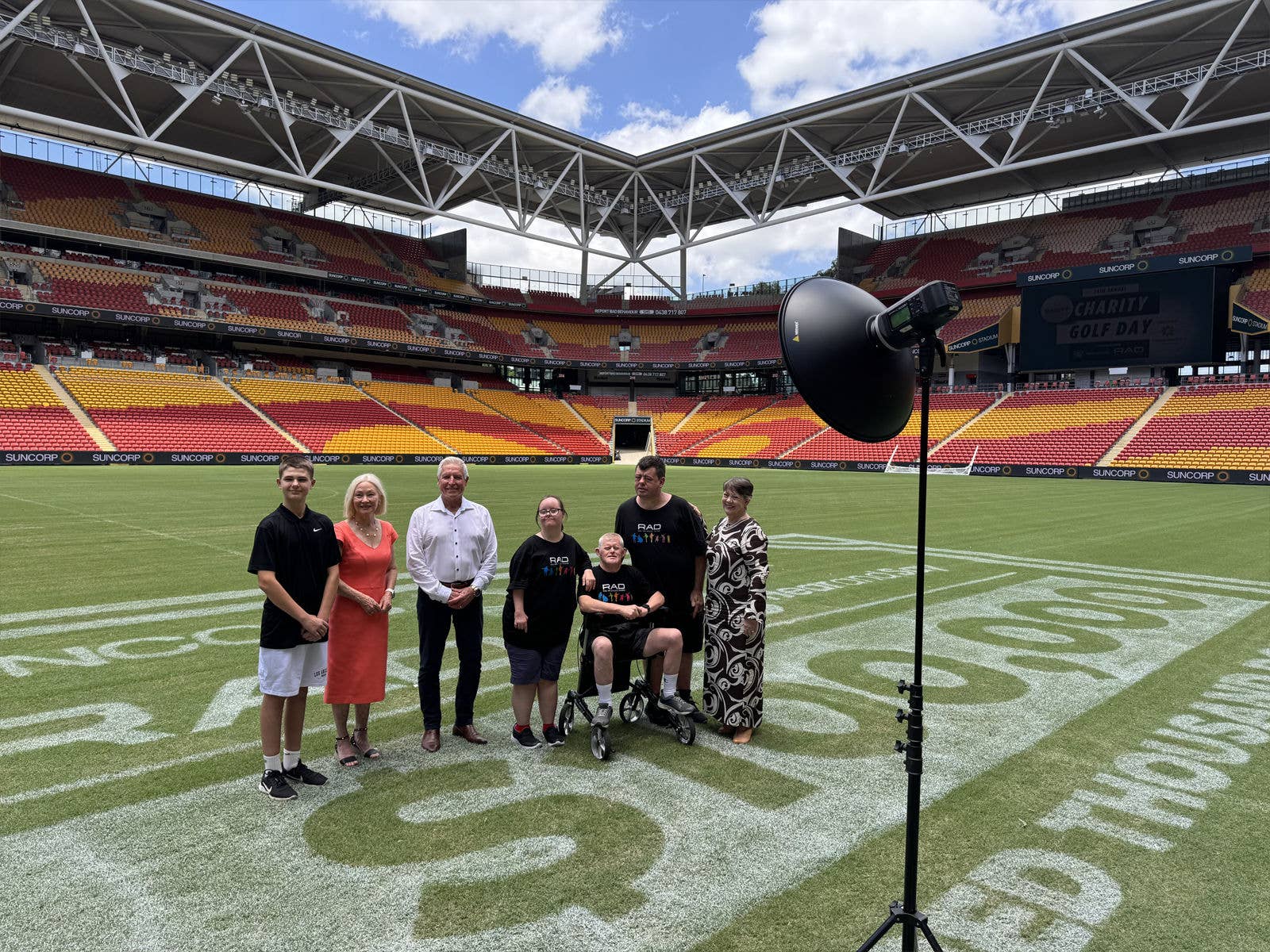 A group of people from Suncorp Stadium, Hear and Say and Centrecare's RAD Inclusive Theatre standing on a giant cheque on the field