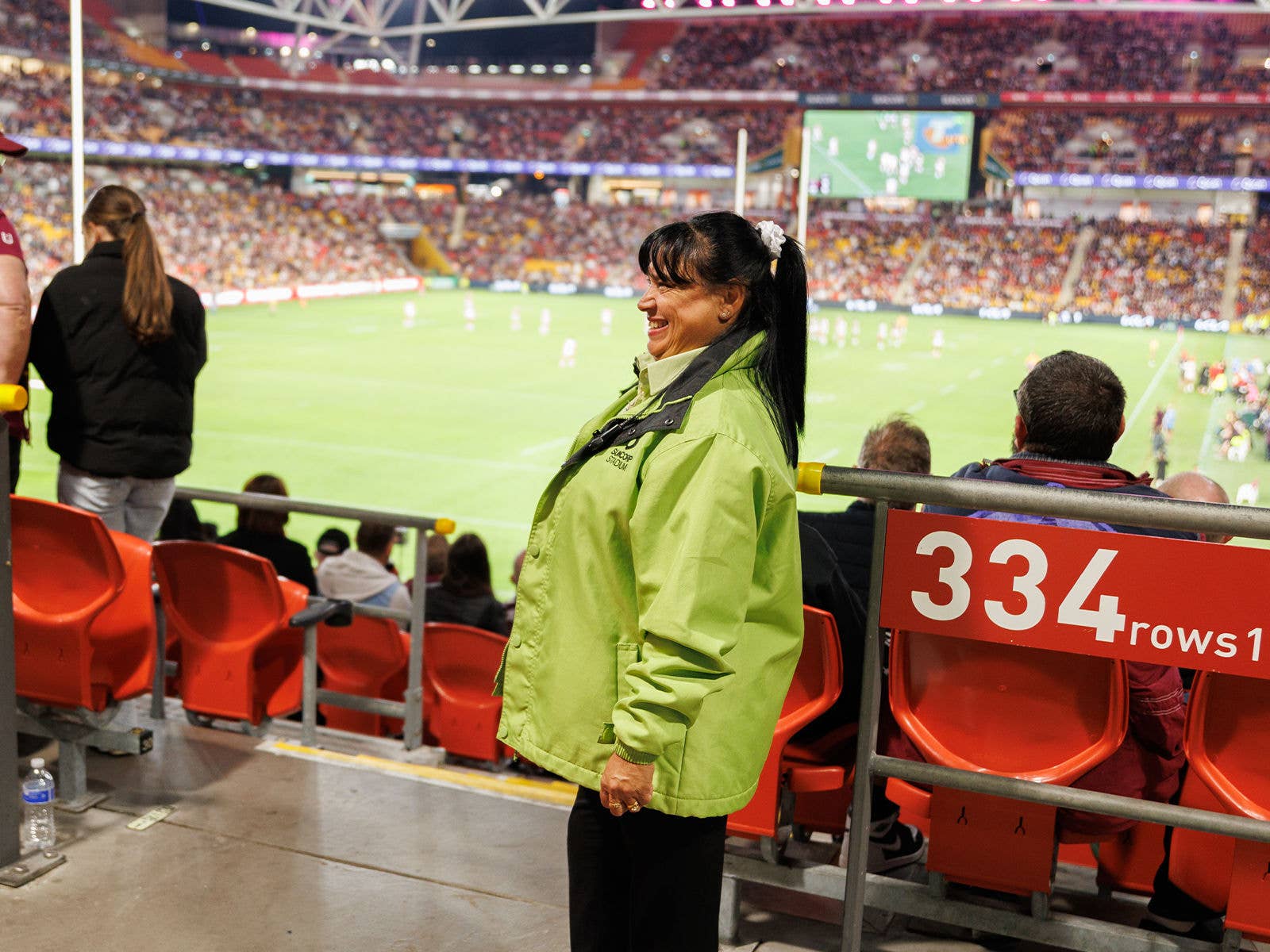 A Suncorp Stadium event staff member smiling at patrons at the top of the aisle Section 224