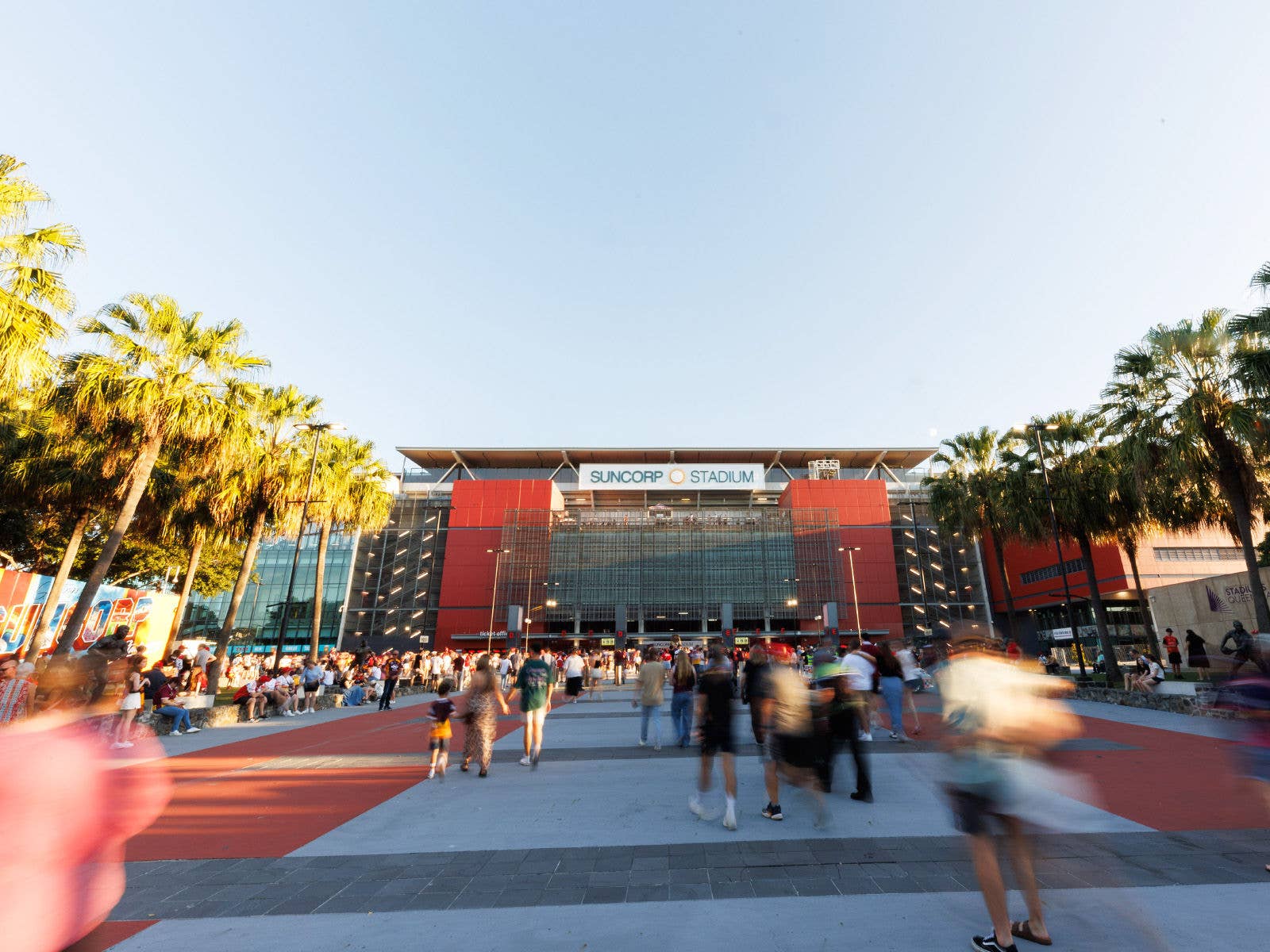 Crowd gathered at the northern plaza entrance of Suncorp Stadium on a sunny day, taken from the perspective of Caxton Street.