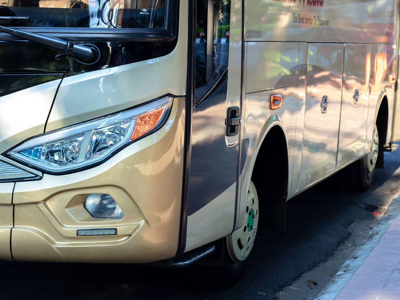 The side of a gold bus parked parallel to the curb