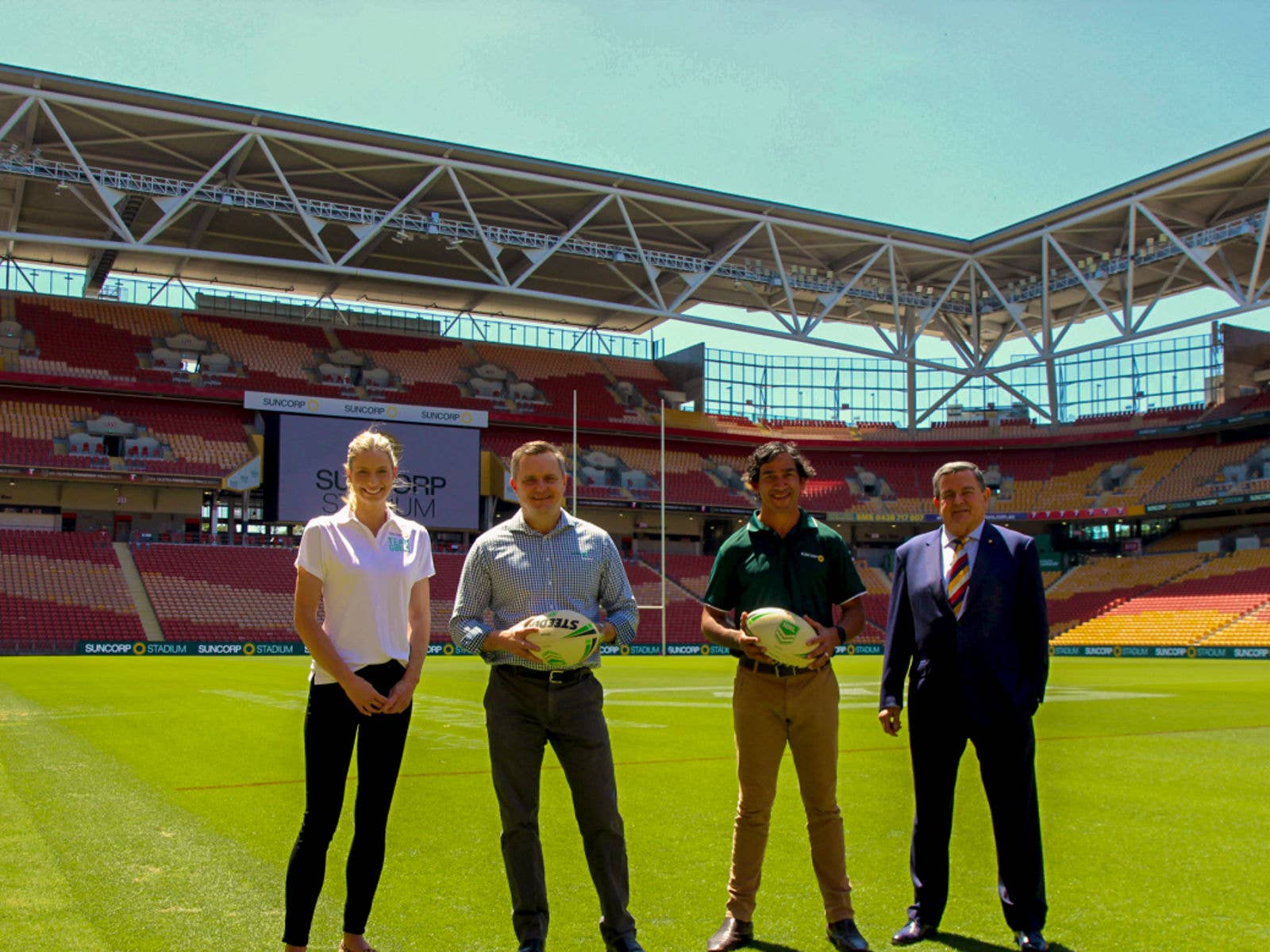Suncorp Renews It's Partnership with the Stadium for up to 10 More Years. Image of Suncorp Ambassador Laura Geitz (Far Left), Suncorp Group CEO Steve Johnston (Left), former NRL Player Johnathan Thurston (Right) and ASM Global Asia Pacific Chairman and Chief Executive Harvey Lister AM (Far Right) on Suncorp Stadium's field. Johnson and Thurston are both holding footballs.
