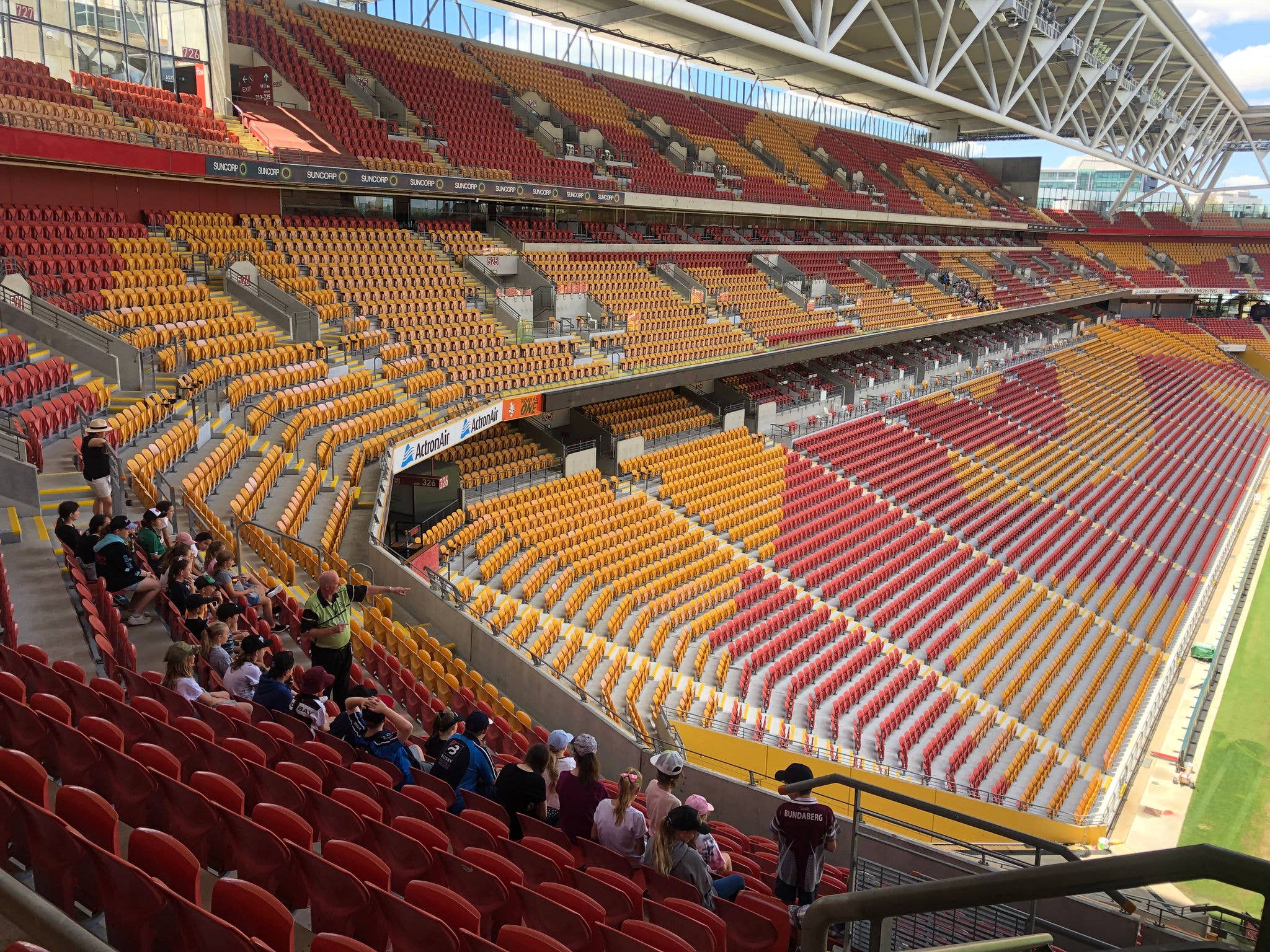 Tour group sitting on Level 5 looking out onto the Suncorp Stadium field where the Tour Guide is pointing.