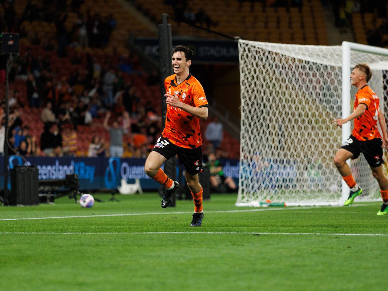 A Brisbane Roar player running and smiling after scoring a goal in a match played at Suncorp Stadium