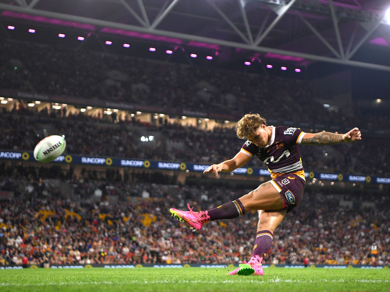 Broncos player Reece Walsh kicking a goal in front of a full Suncorp Stadium crowd