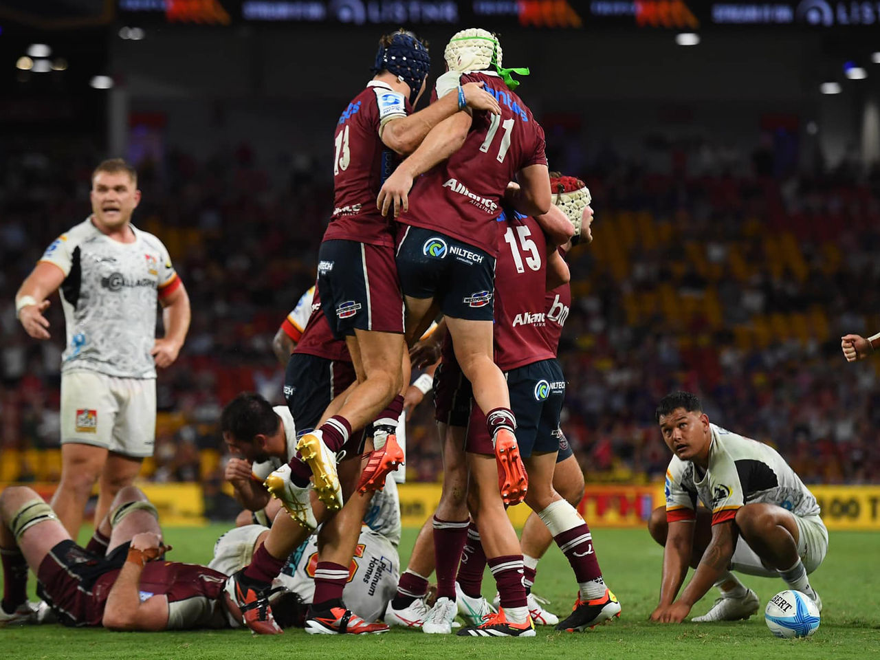 Image of multiple Queensland Reds players jumping in the air, mid celebration, during a game. The opposing team is watching them.