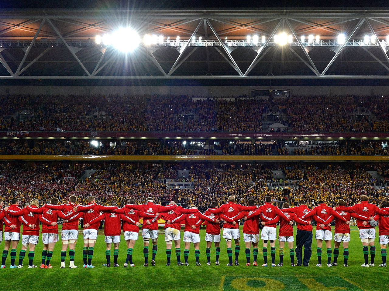 Image of British and Irish Lions players lined up, linking arms, facing out into a crowded Suncorp Stadium, during the national anthem.