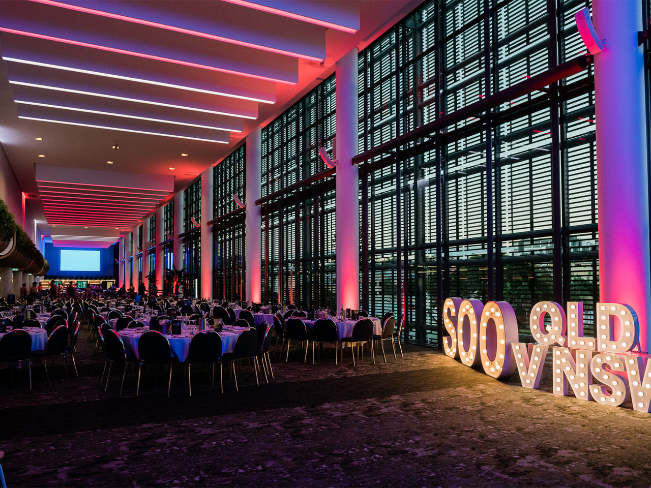 A wide shot of the room before the Members State of Origin Dining Function with it all dressed up and themed blue and maroon with a neon sign saying 'SOO QLD v NSW'