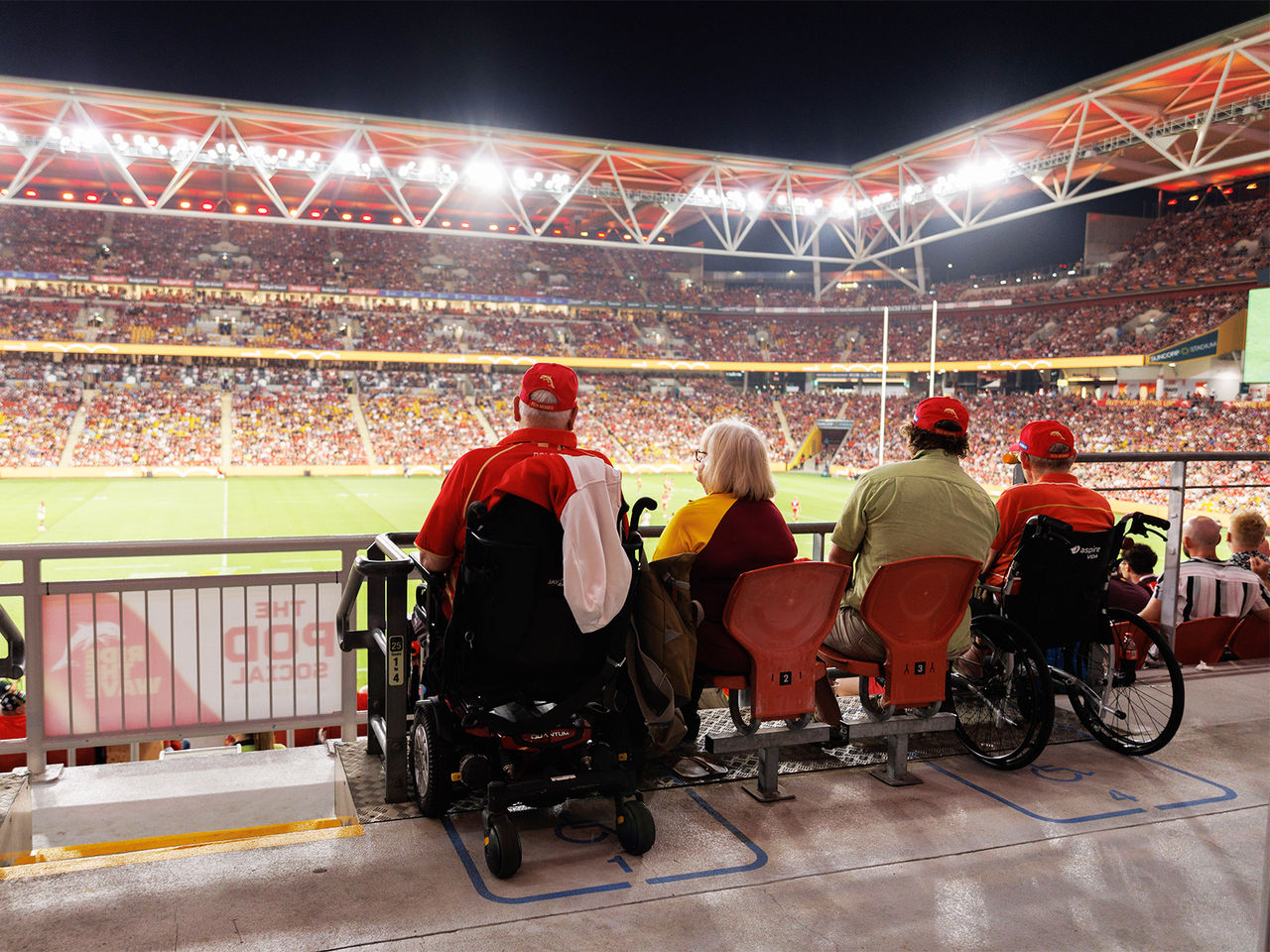 Four patrons sat in the Accessible seating area at Suncorp Stadium watching a nighttime game.