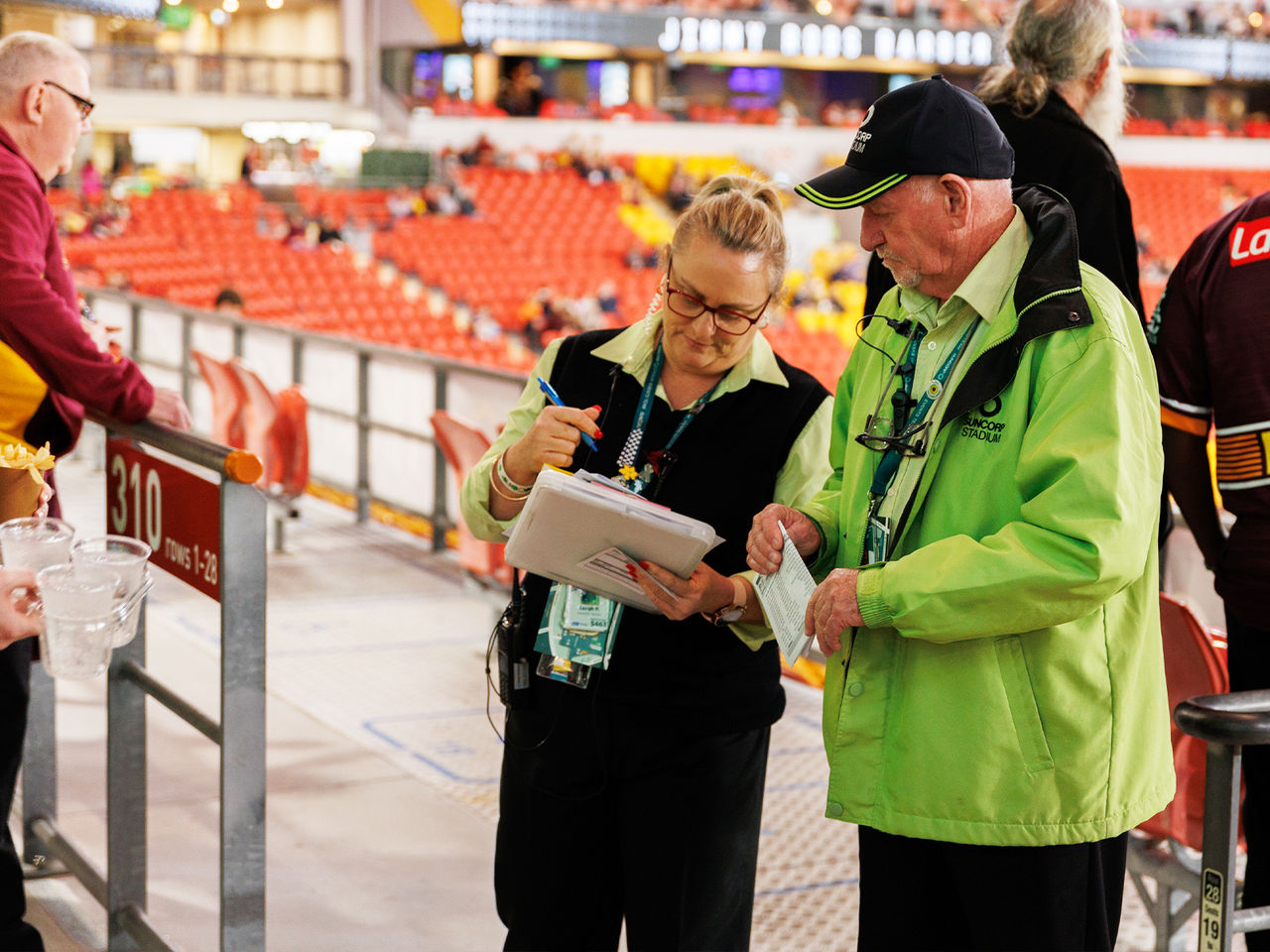 Image of two Suncorp Stadium staff members looking at a folder whilst stood on the Suncorp Stadium concourse.